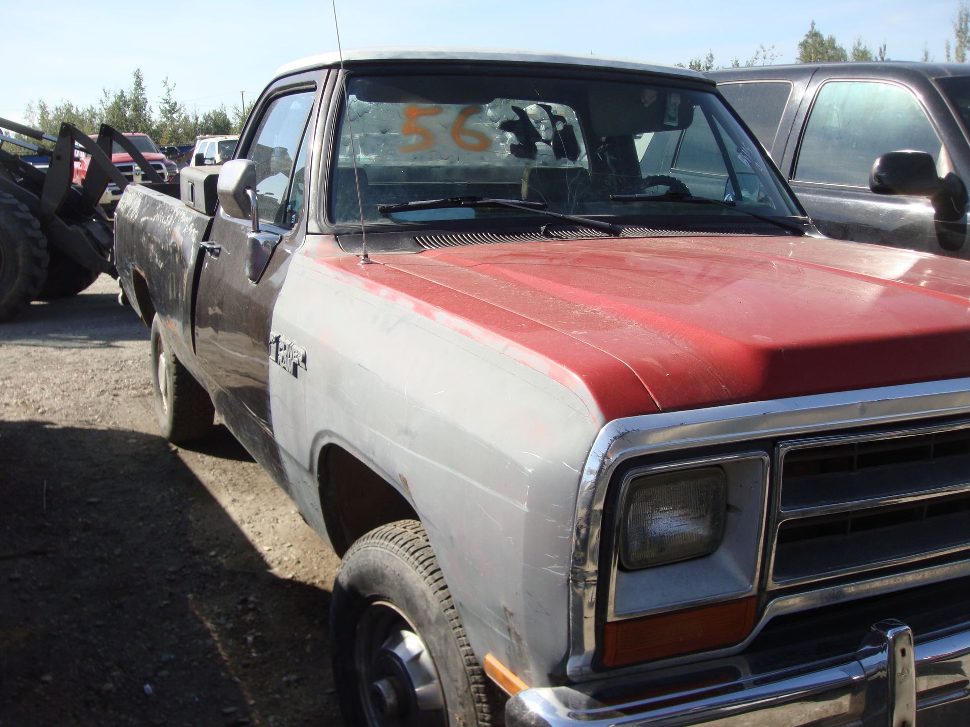 Old pickup truck with red hood and gray body parked in a used car lot
