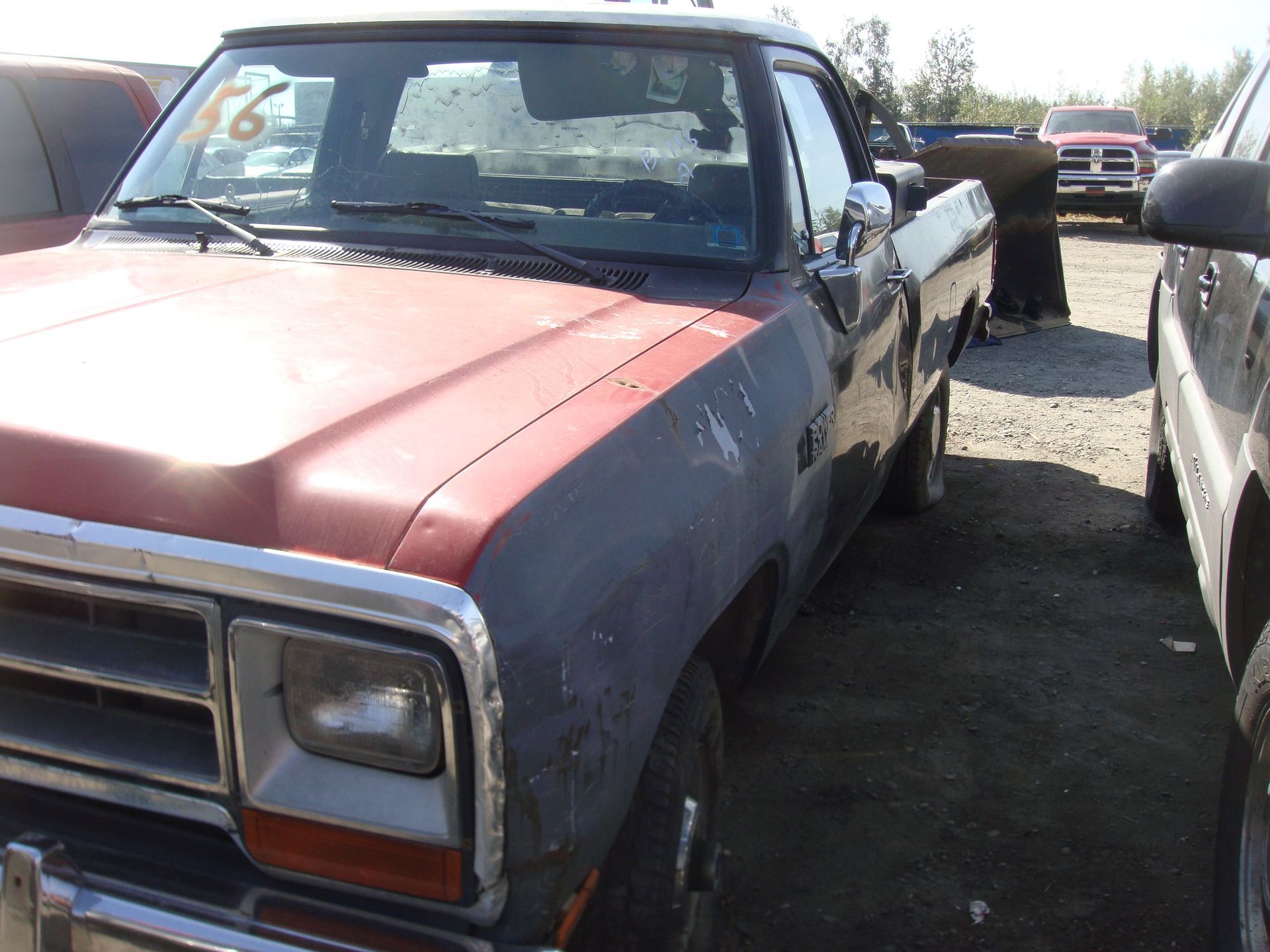 Red and blue pickup truck parked in a row of vehicles on a gravel lot.