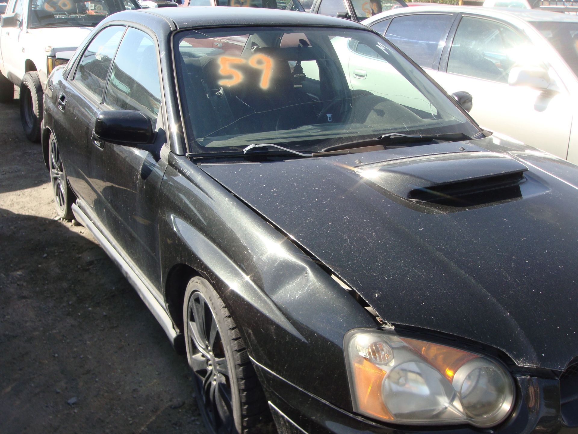 Black sports sedan parked outdoors with orange “57” on windshield and hood scoop
