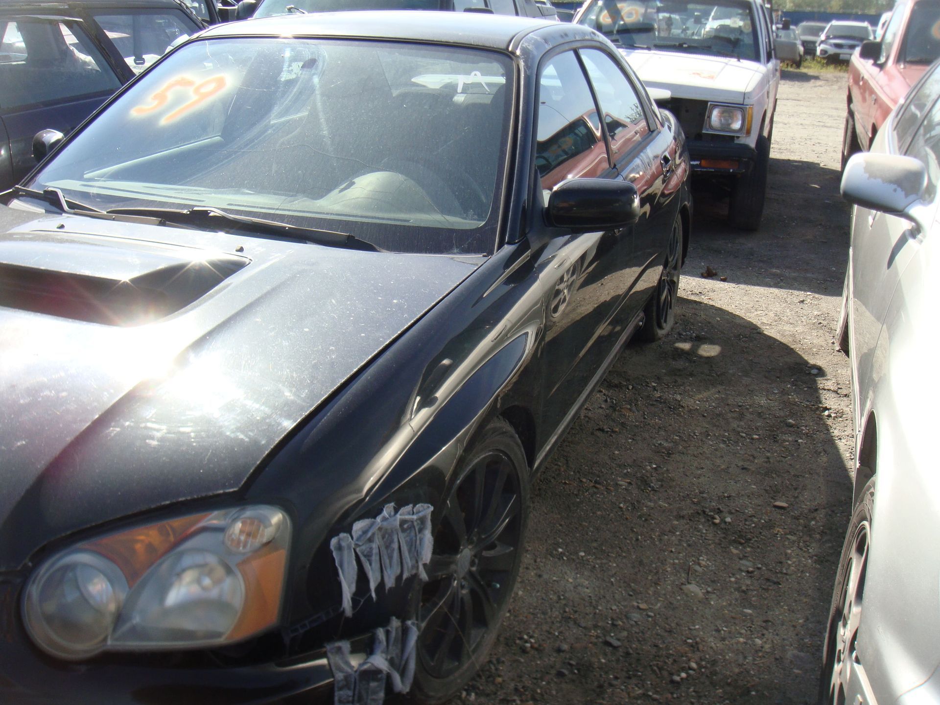 Black sports coupe parked in a crowded lot, front-left view, with damage on the front bumper