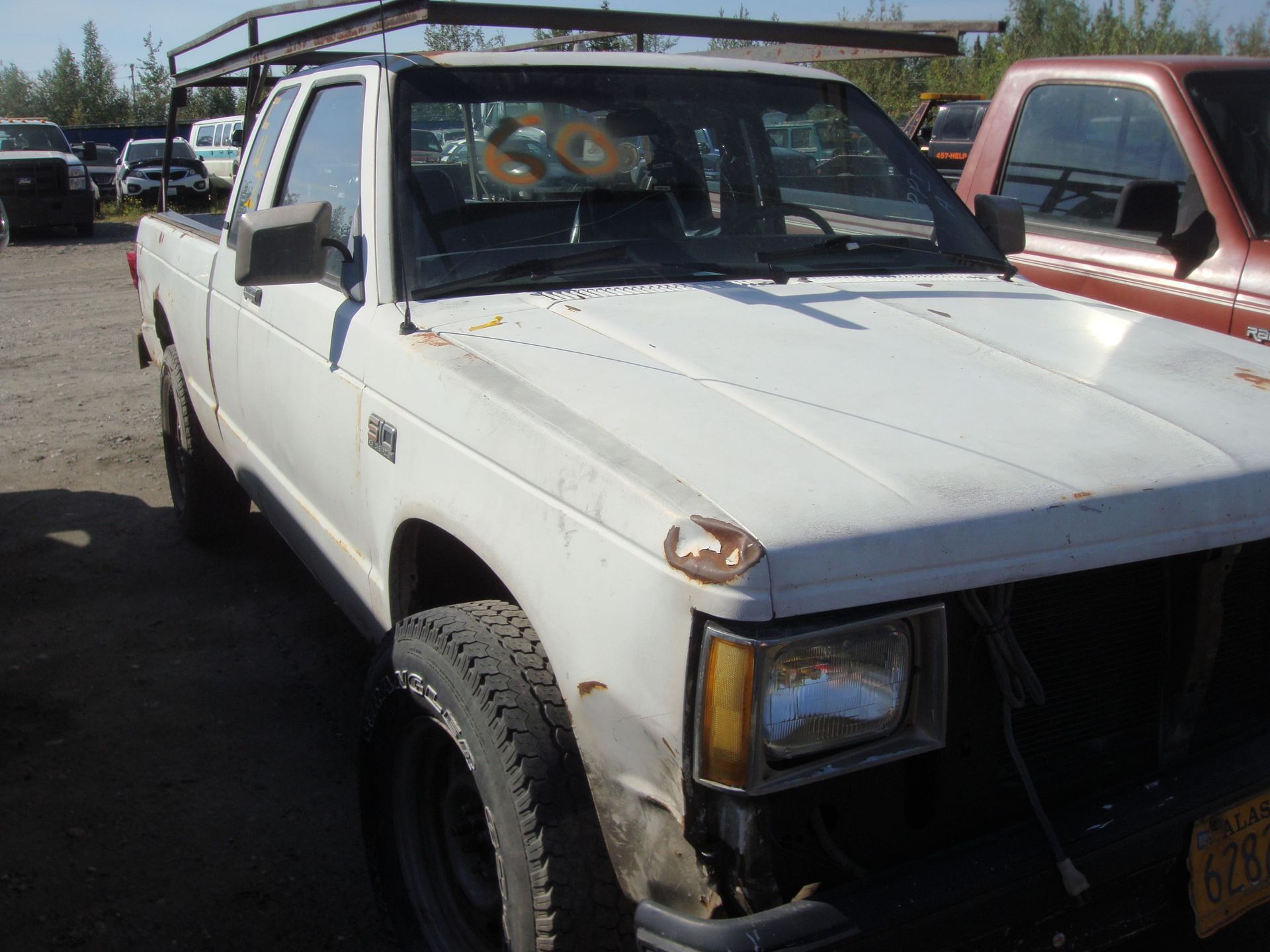 White pickup truck parked in a lot, with visible front damage and a red truck beside it