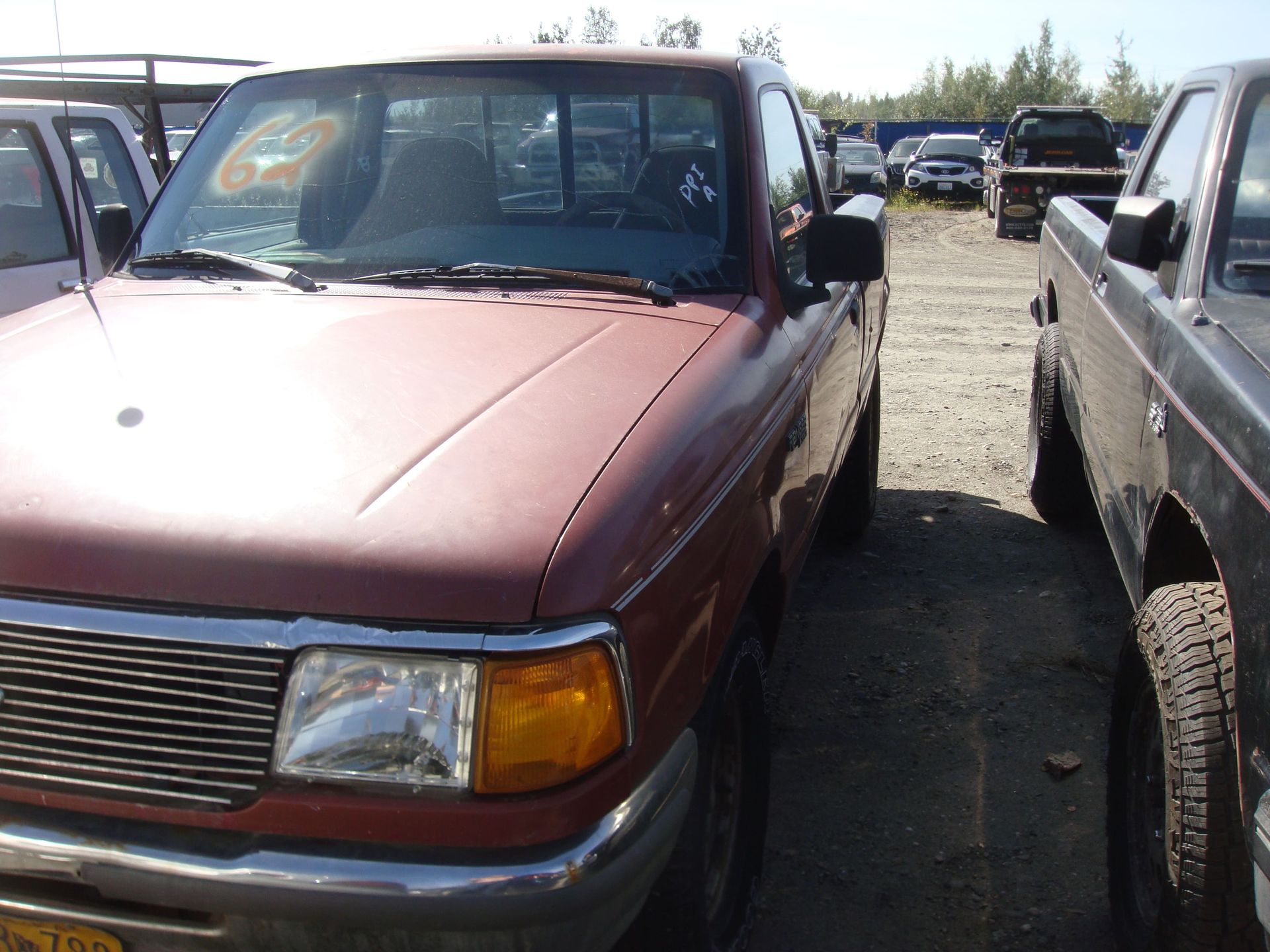Maroon pickup truck parked in a lot between other vehicles.