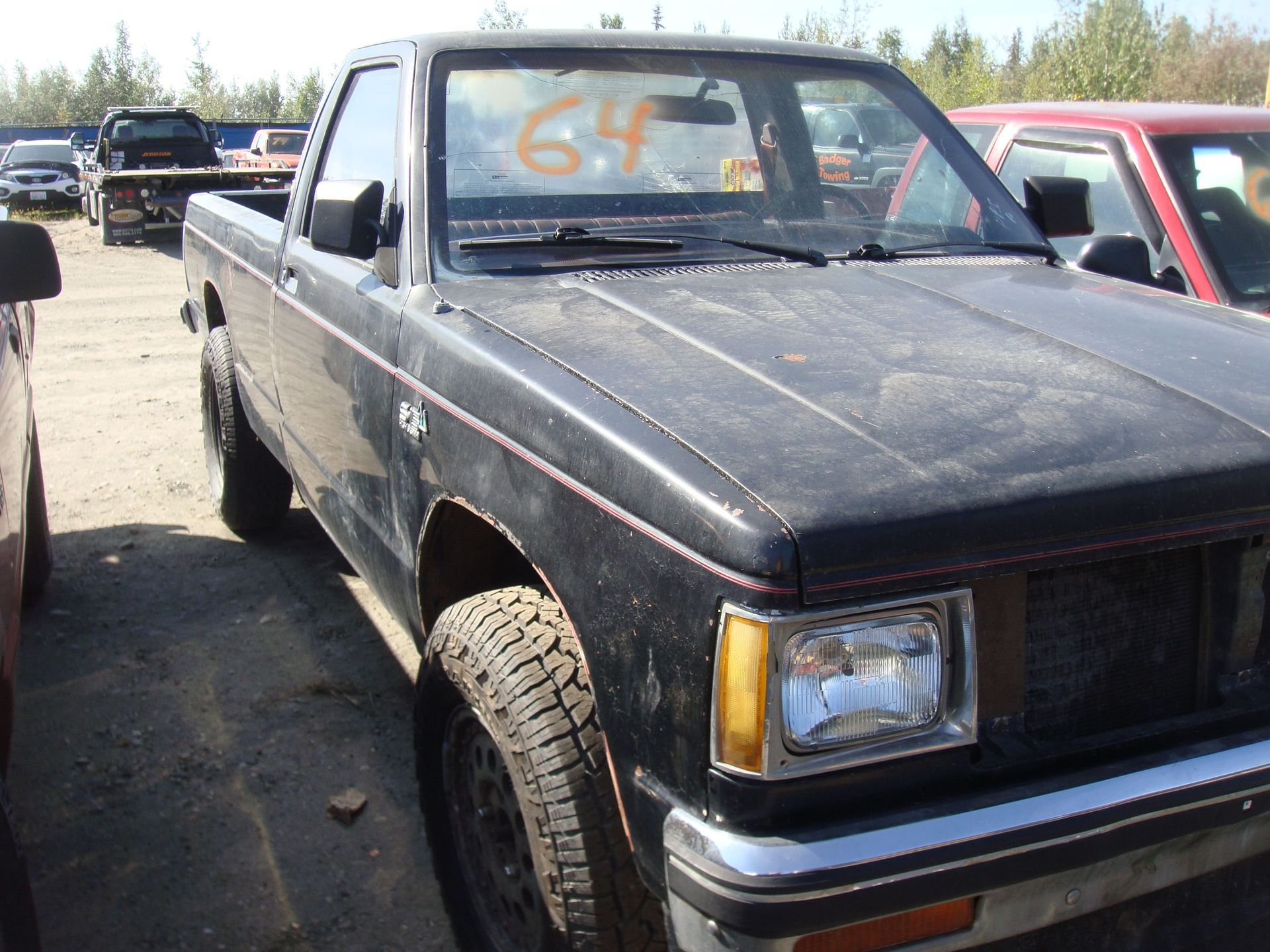 Black pickup truck parked outdoors with a dusty hood and orange price writing on the windshield