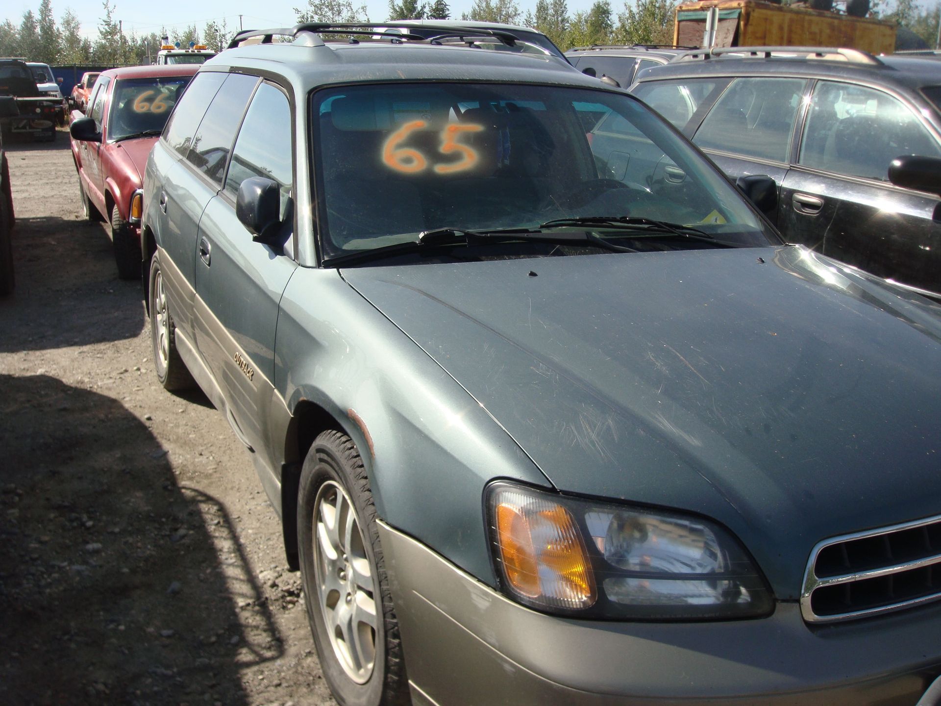 Gray station wagon in a car lot with orange “65” written on the windshield