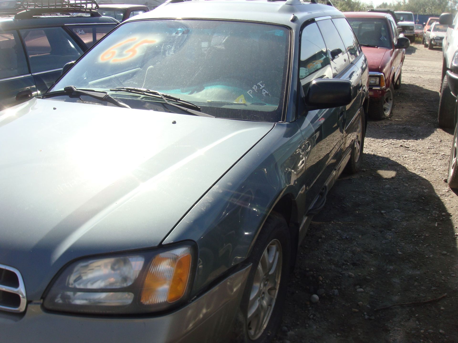 Green SUV parked in a gravel lot beside other cars, with a cracked windshield.