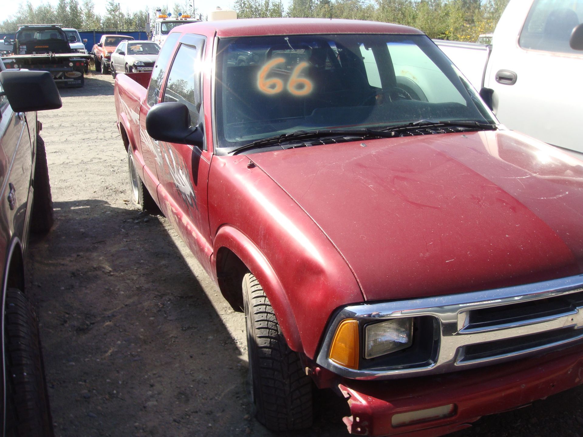 Red pickup truck parked in a gravel lot, with a large 66 visible on the windshield.