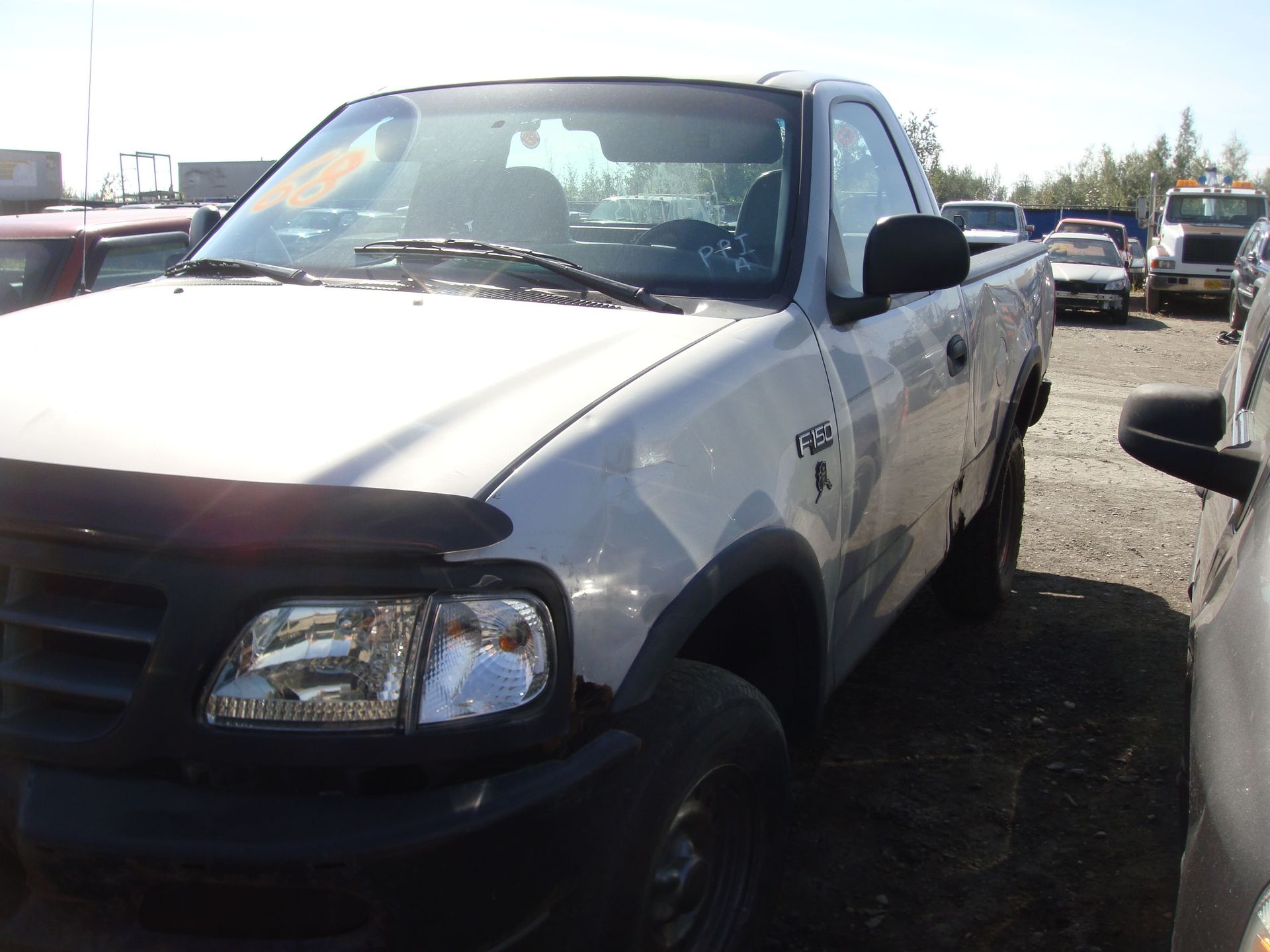 White pickup truck parked in a dirt lot with visible front-end damage and a cracked windshield