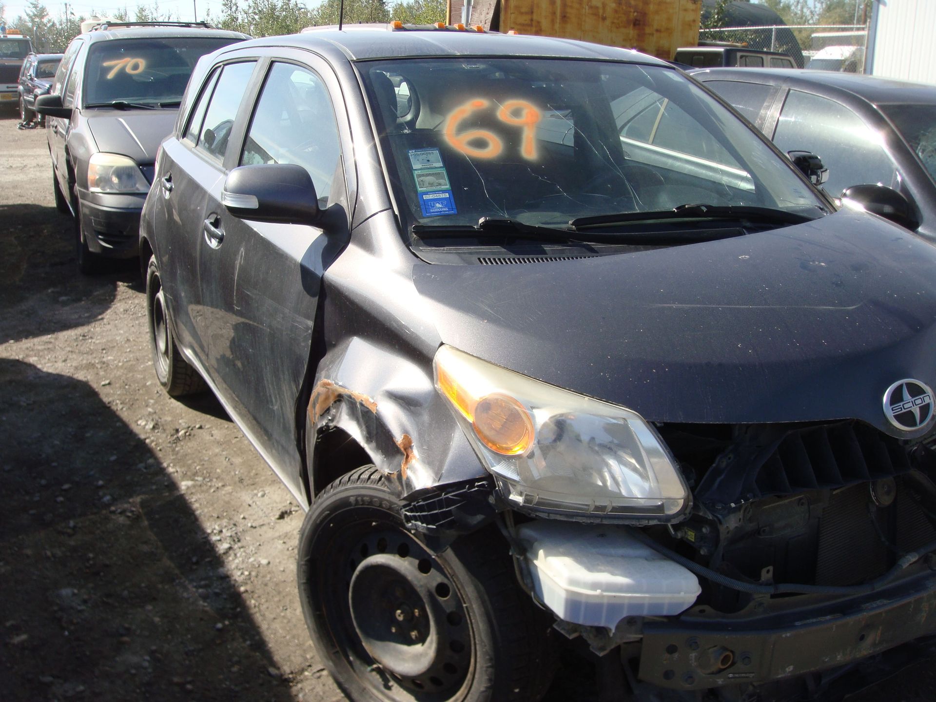 Damaged black compact car with front-end collision, parked in a lot with other vehicles.