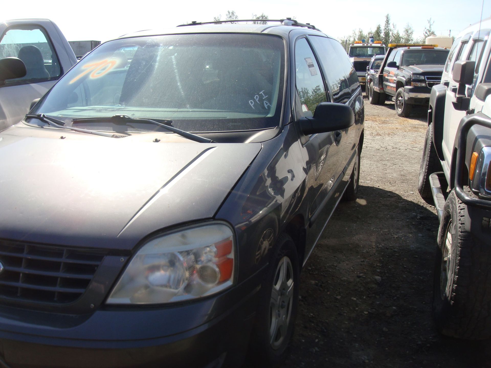 Black minivan parked in a crowded car lot, front view on a gravel surface