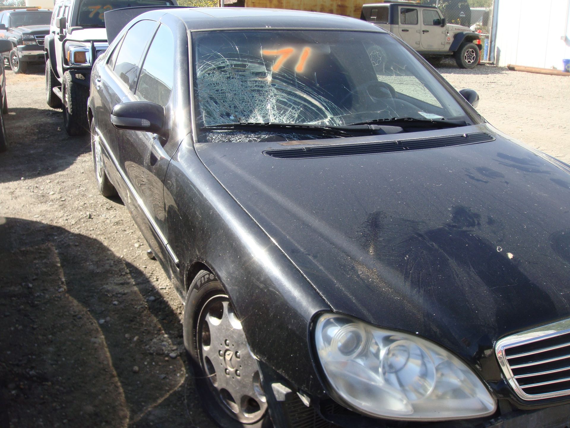 Black sedan with a cracked windshield parked on a street near other cars, number 71 marked on the glass