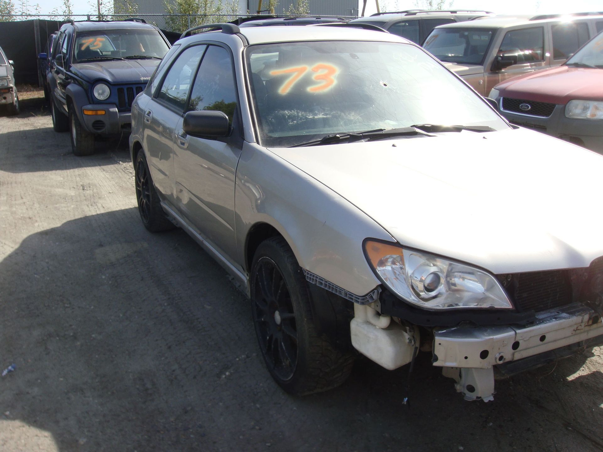 Silver car with front-end damage parked in a lot, marked “79” on the windshield.