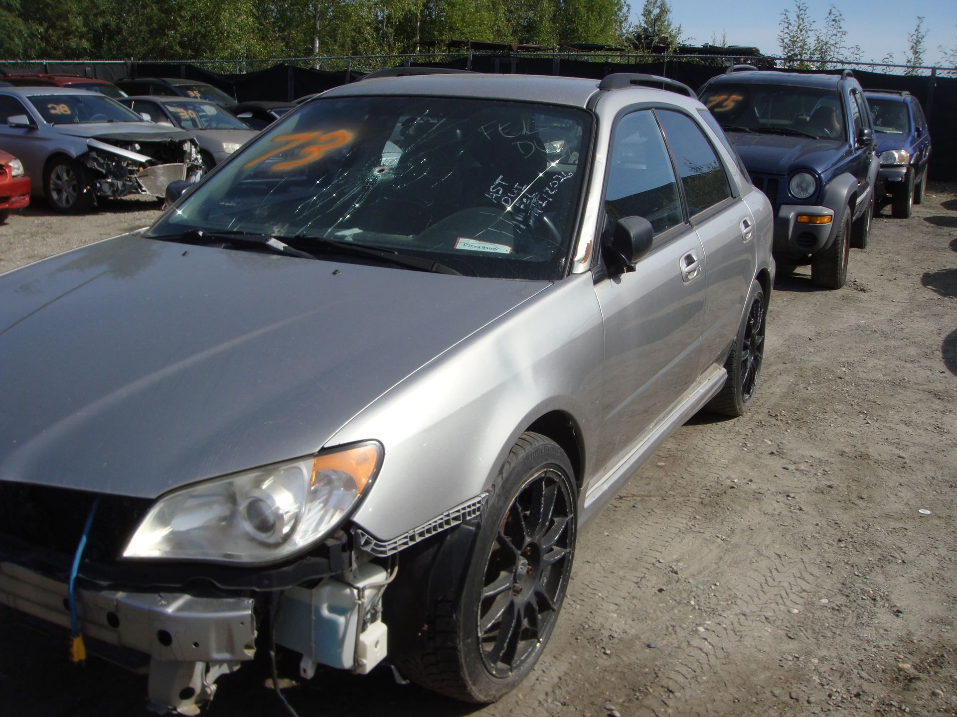 Silver sedan with front-end damage parked in a lot beside other vehicles