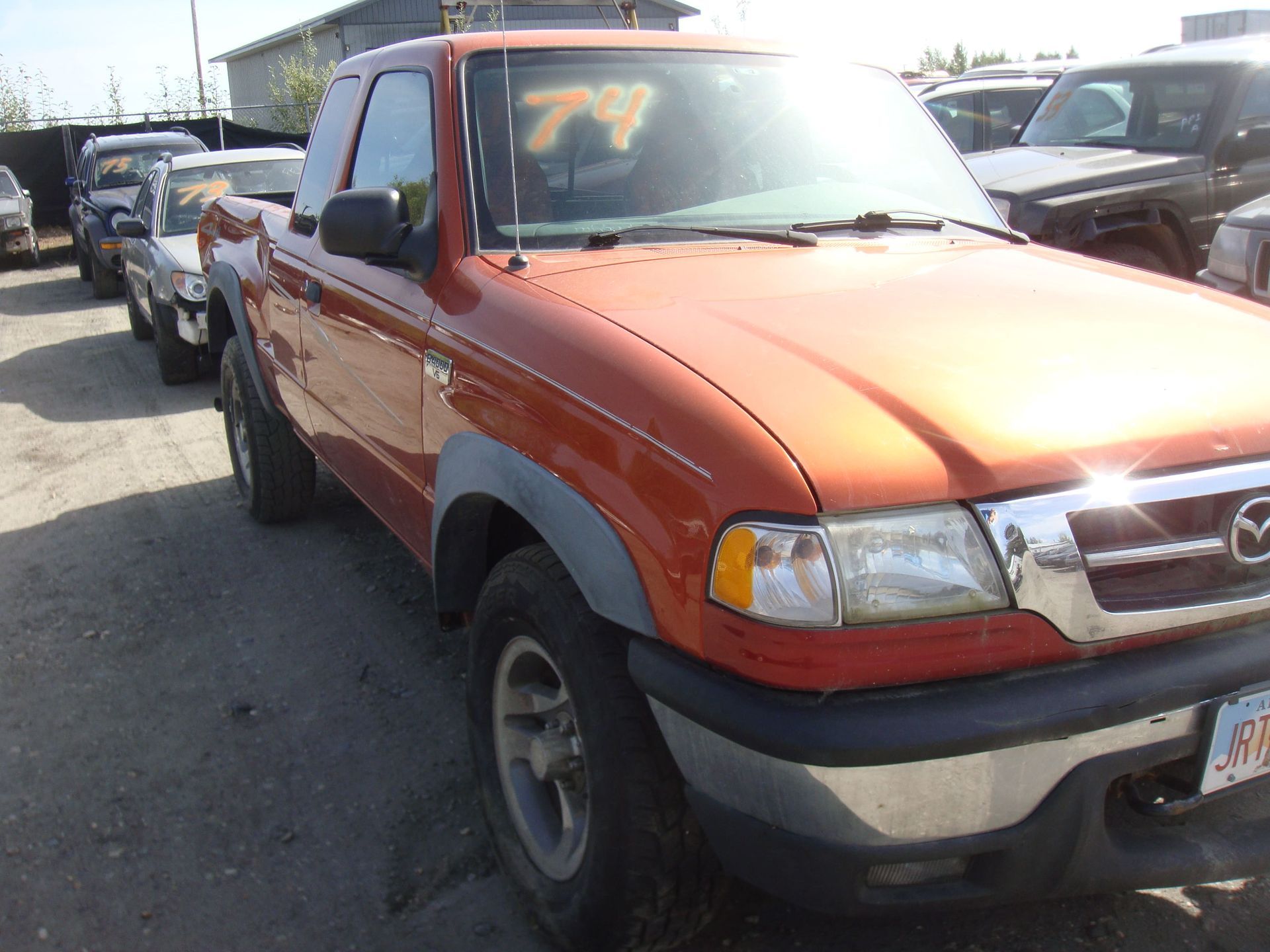 Orange Mazda pickup truck parked in a row of used cars on a sunny lot