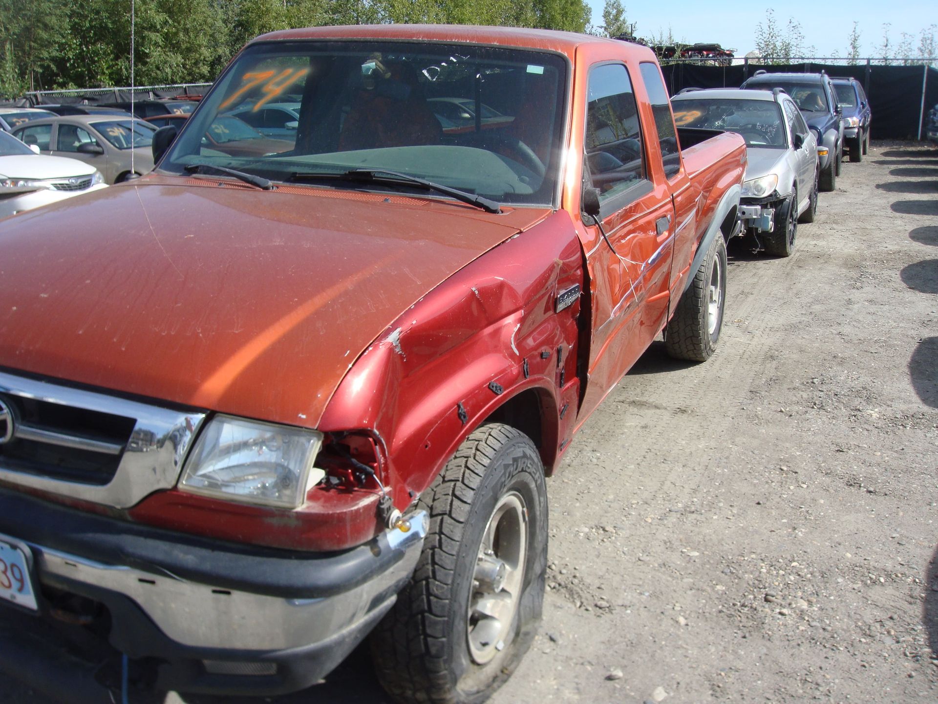 Damaged red pickup truck parked in a dusty lot with other vehicles nearby
