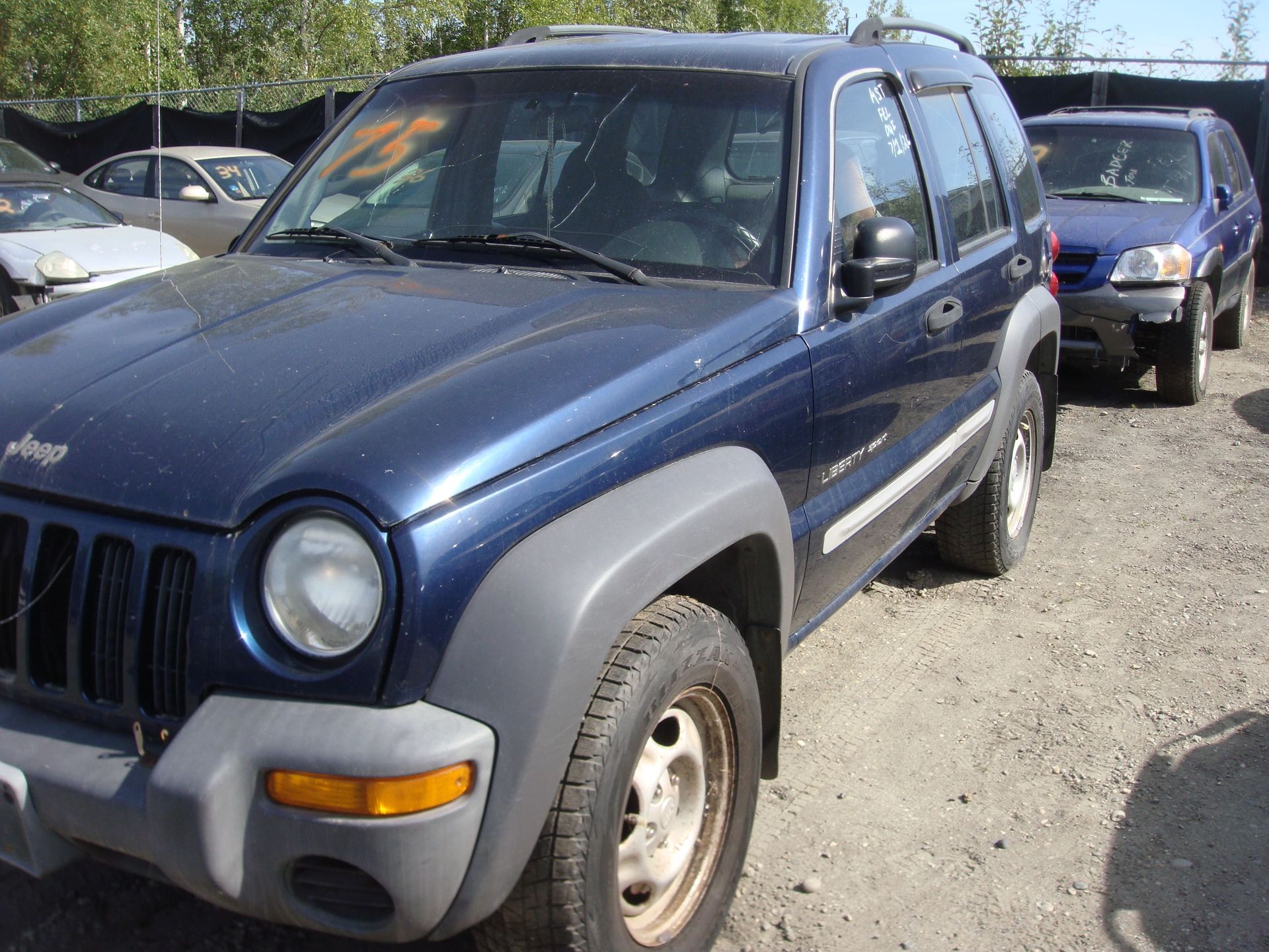 Blue SUV parked in a gravel lot, with another vehicle behind it.