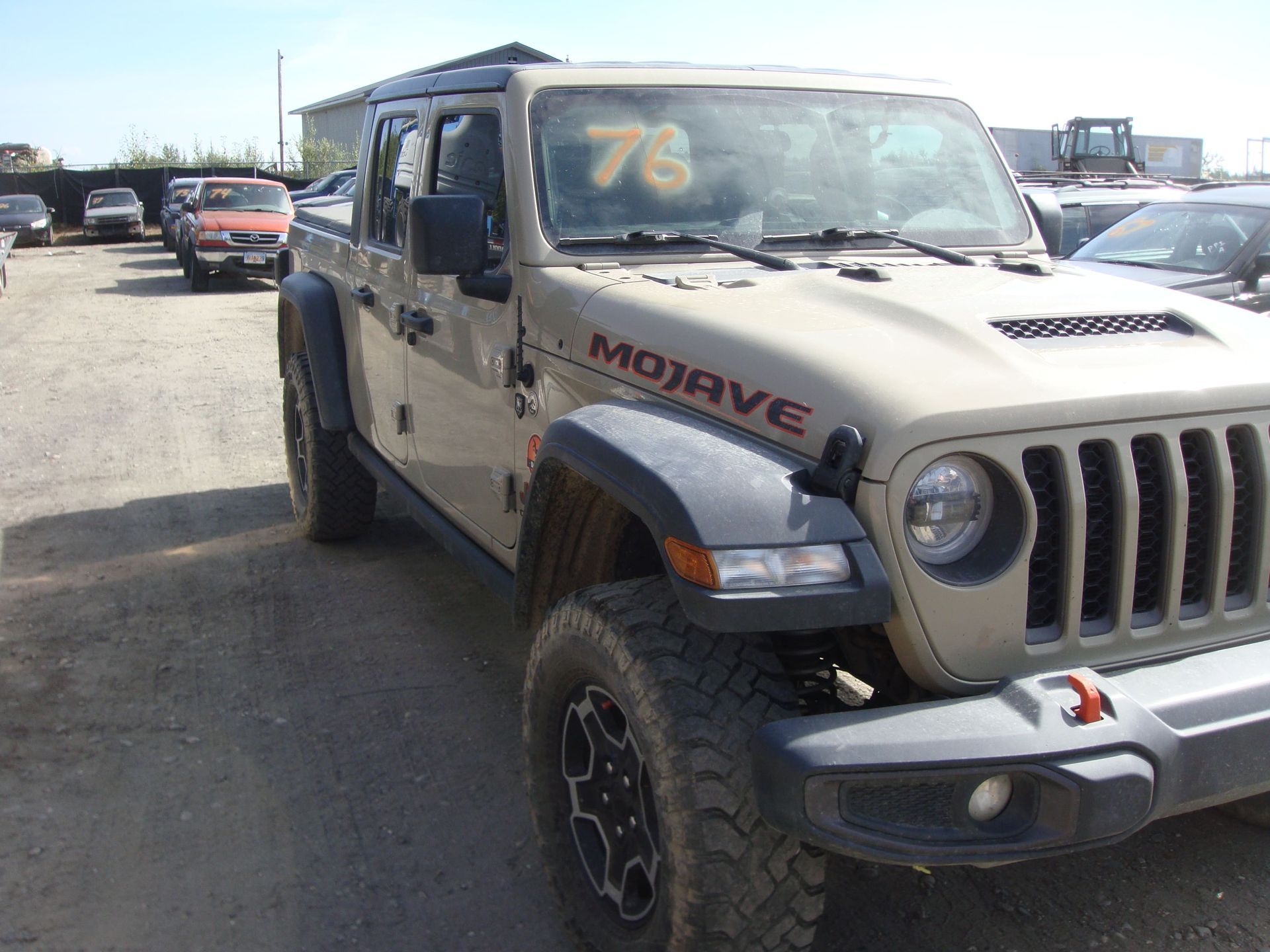 Beige Jeep Wrangler parked in a lot, angled front view with black fenders and “MOJAVE” decal.
