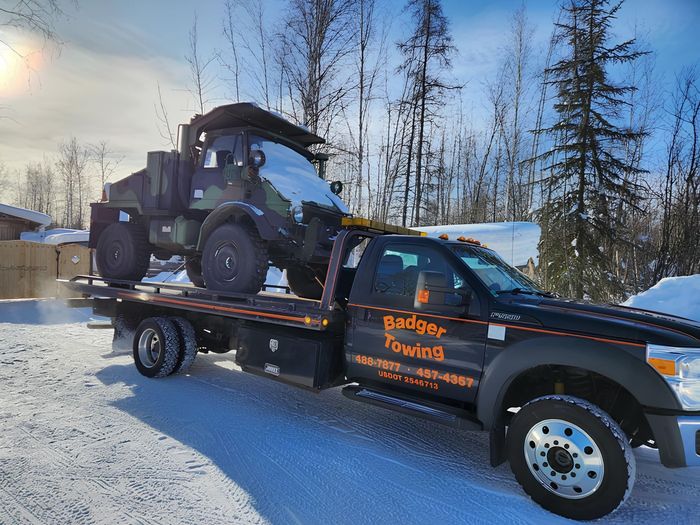 a badger towing truck is carrying a yellow deere bulldozer