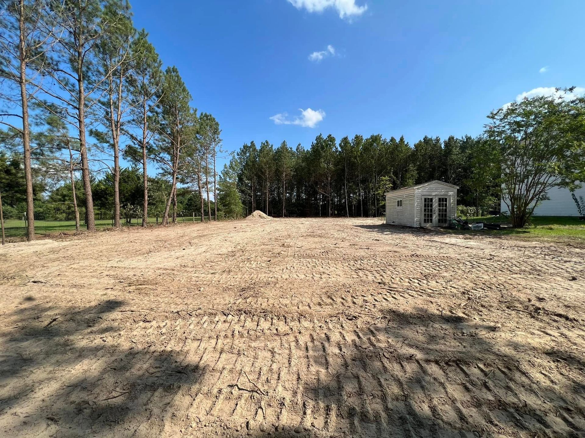 A large, vacant dirt lot cleared for development, with a small shed in the distance under a clear blue sky.