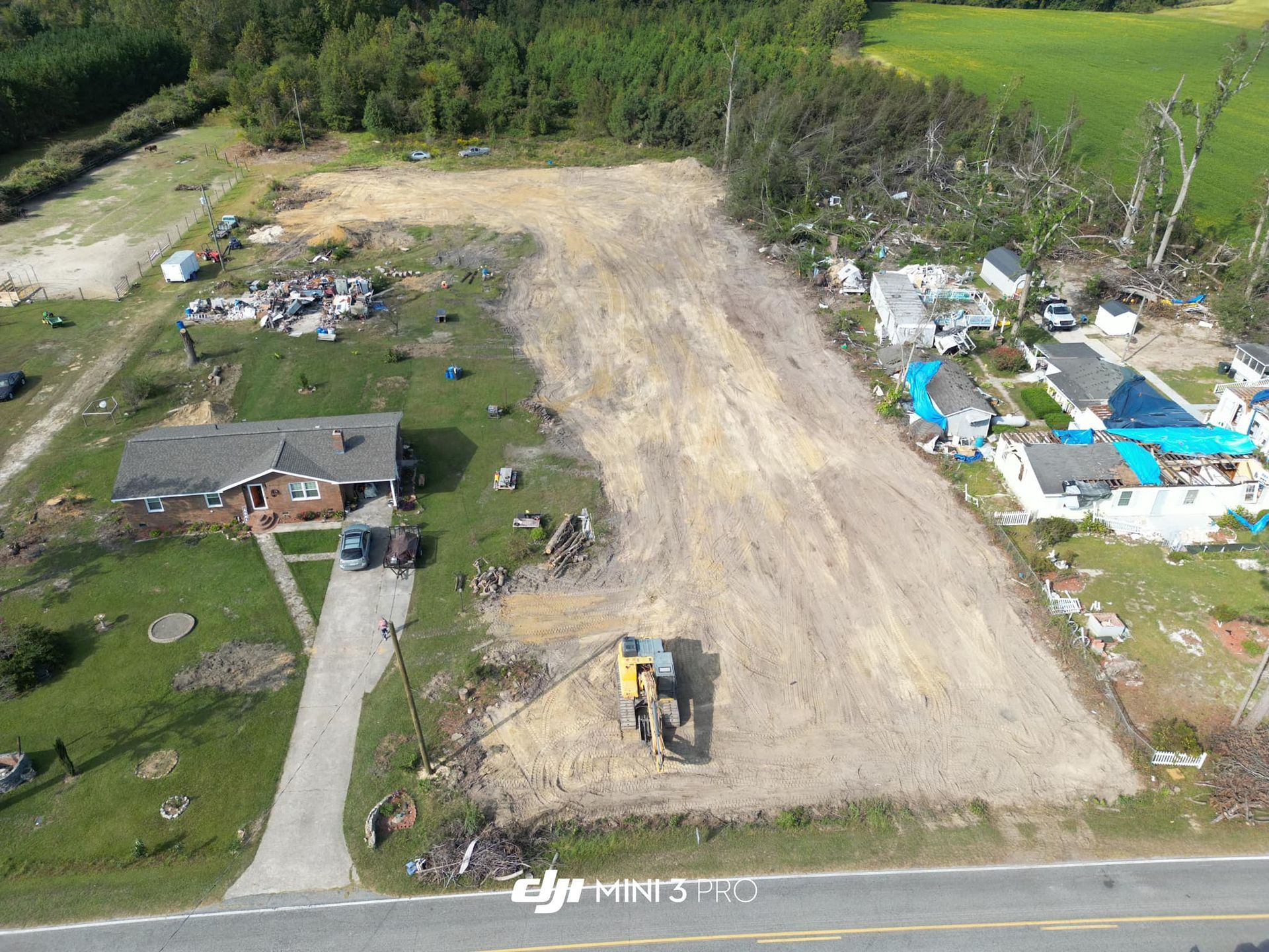 Aerial view of a cleared dirt lot beside homes, with a bulldozer and trees in the background.