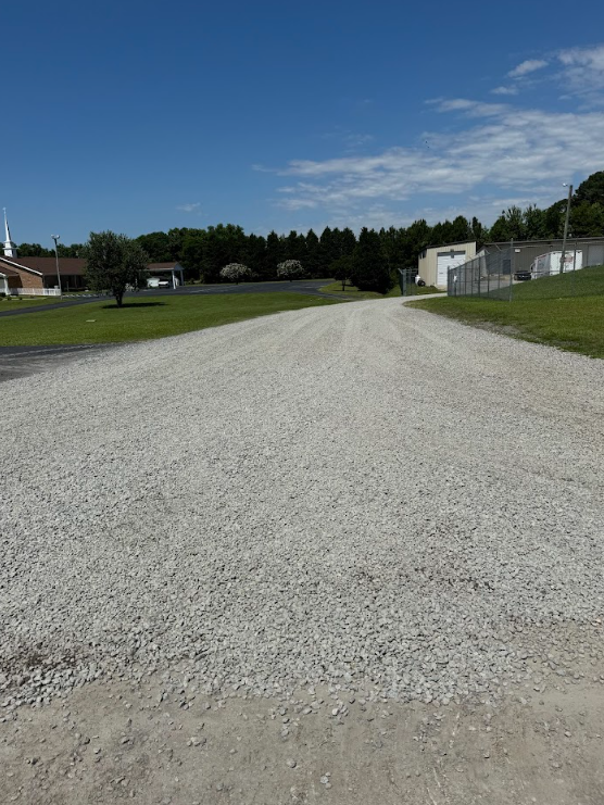 Gravel road leading through a grassy park under a blue sky with scattered clouds