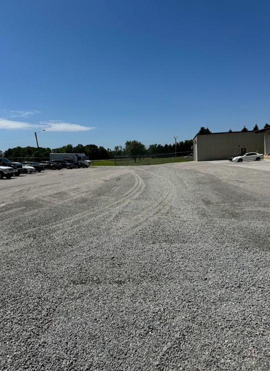 Gravel parking lot under a clear blue sky, with parked cars on the left and a building on the right