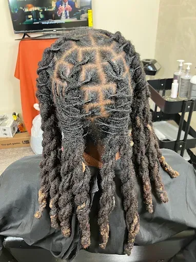 Close-up of long twisted braids from the back in a salon chair, with a TV in the background.