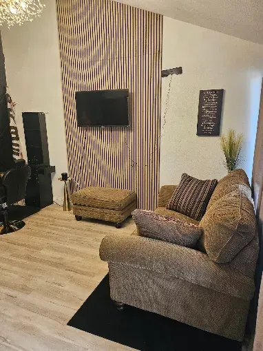 Modern living room with gray sofa, wall-mounted TV, striped accent wall, and black rug