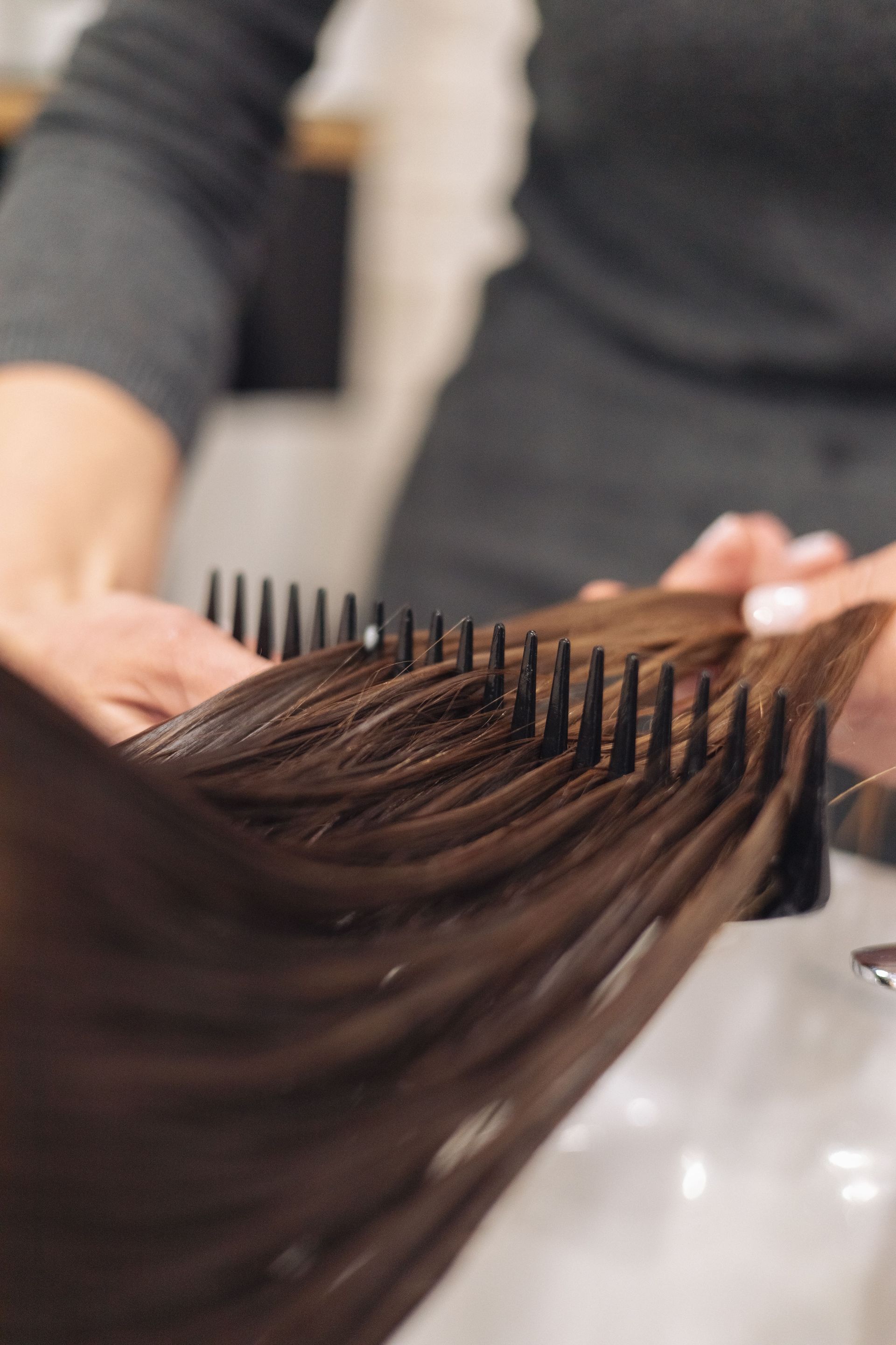Hairdresser combing long brown hair in a salon