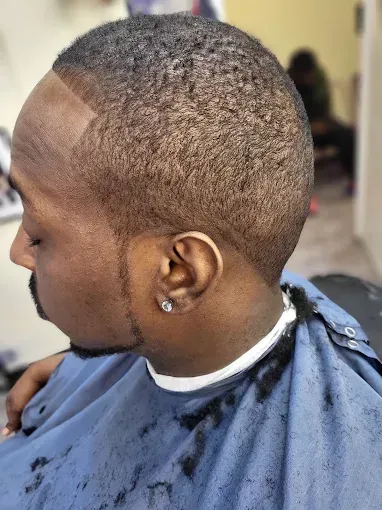 Side-profile haircut with a close fade and short textured top, in a barbershop chair.