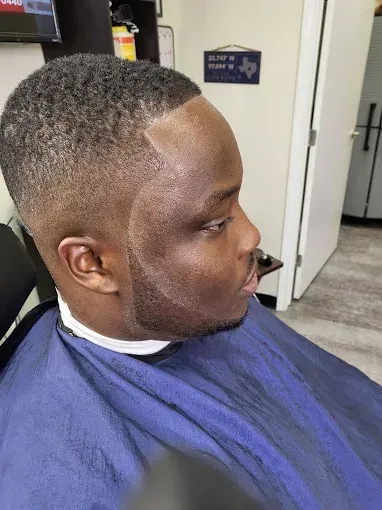 Man with a short fade haircut seated in a barber chair wearing a blue cape, side profile.