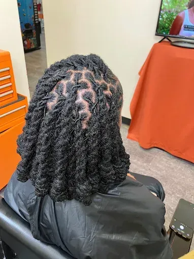 Person with twisted braids seated in a salon chair, seen from behind near a styling station.