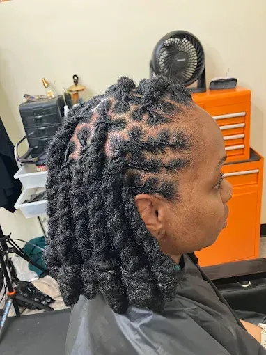 Side view of a person with twisted braids sitting in a salon chair, with orange tool cabinets behind them.