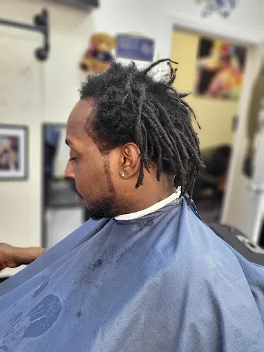 Man in a barber chair with blue cape, side profile, in a barbershop.
