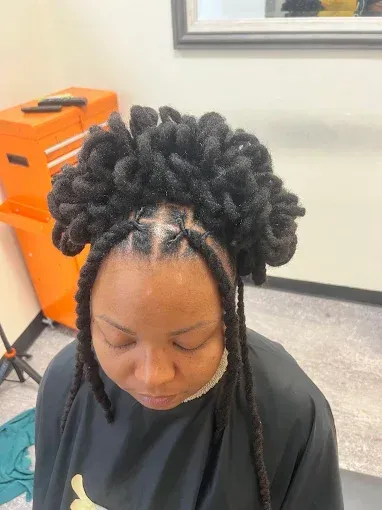 Person with styled braided hair looking down in a salon chair, with orange equipment in the background.