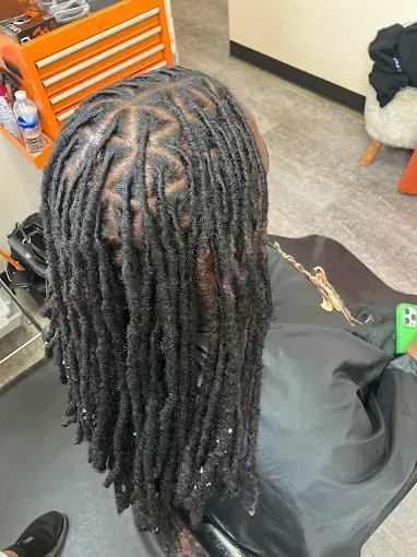Person with long black locs seated in a salon chair, seen from above.