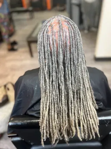 Back view of long silver braided hair in a salon chair, with pink highlights at the crown