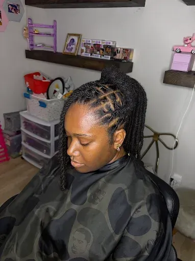 Woman with braided ponytail sitting in a chair, wearing a black cape in a home salon room.