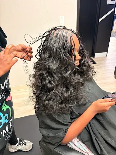Person with long curly hair sitting in a salon chair while another person styles their hair