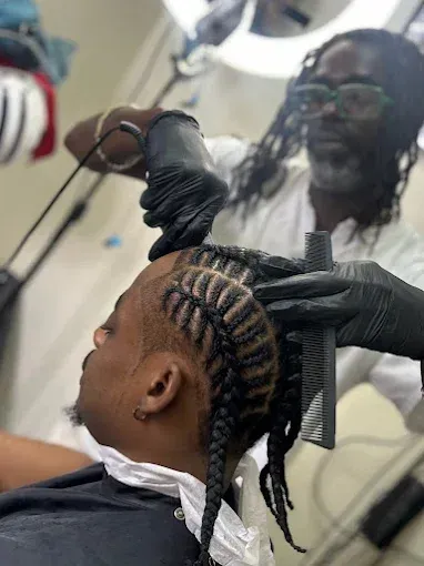 Hair stylist braiding a client’s hair in a salon, with a mirror reflecting the stylist.