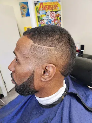 Side profile of a man with a fresh fade haircut in a barber chair, wearing a blue cape and neck strip.