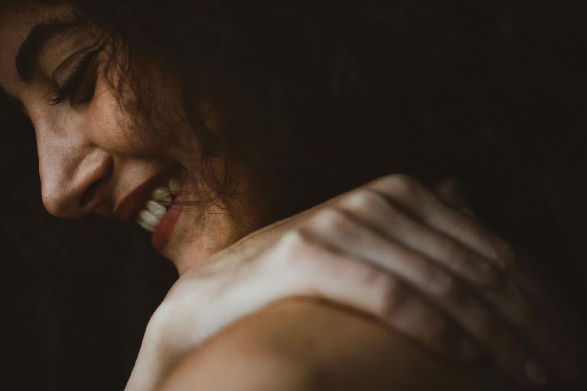 Close-up of a smiling person resting their head on folded arms in warm, dim light
