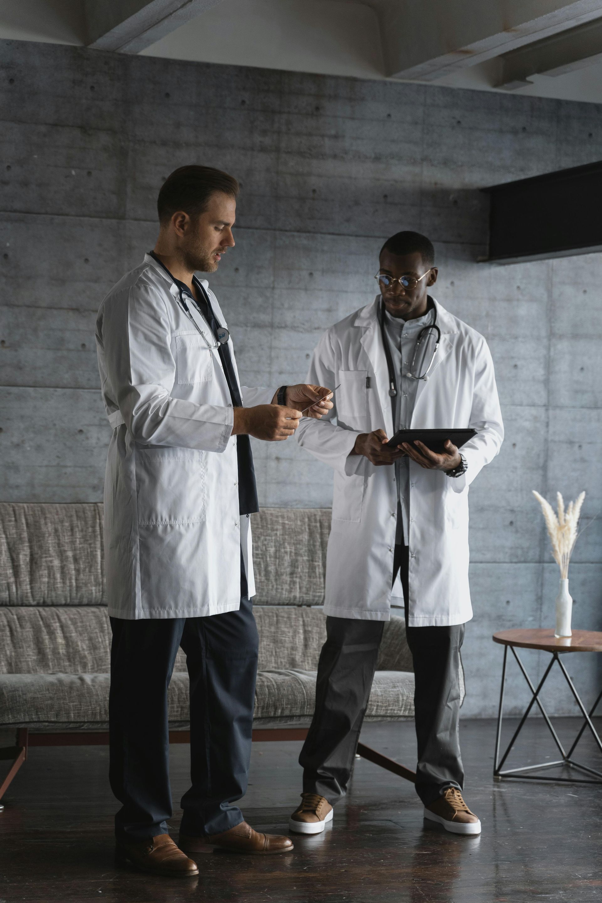 Two doctors in white coats discussing a tablet in a modern concrete room