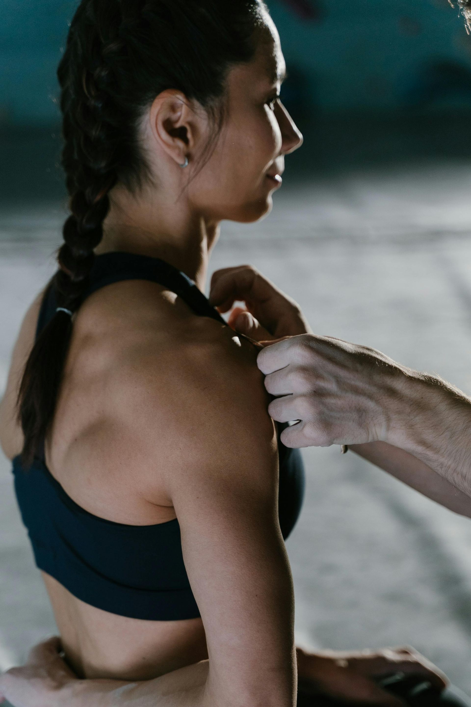 Hands adjusting a black sports bra on a seated woman in a dim gym setting