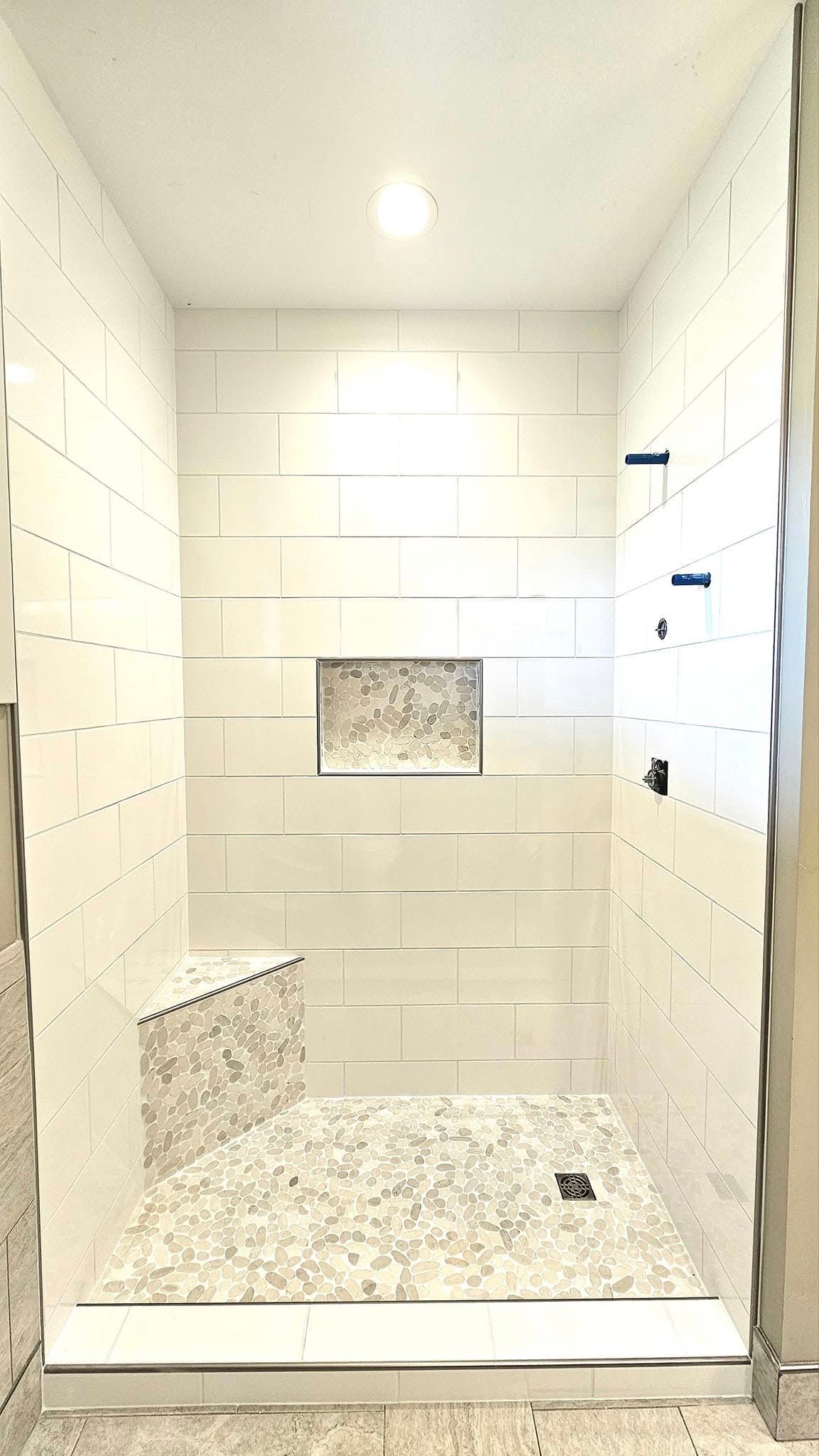 A bathroom with white tiles and a walk in shower.