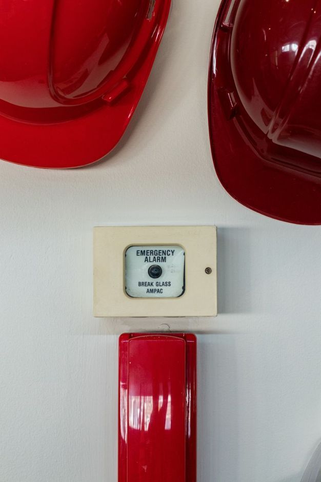 Red Emergency Phone And Break Glass Alarm With Two Red Hard Hats On White Wall — Wendy's Safety Services in Moulden, NT