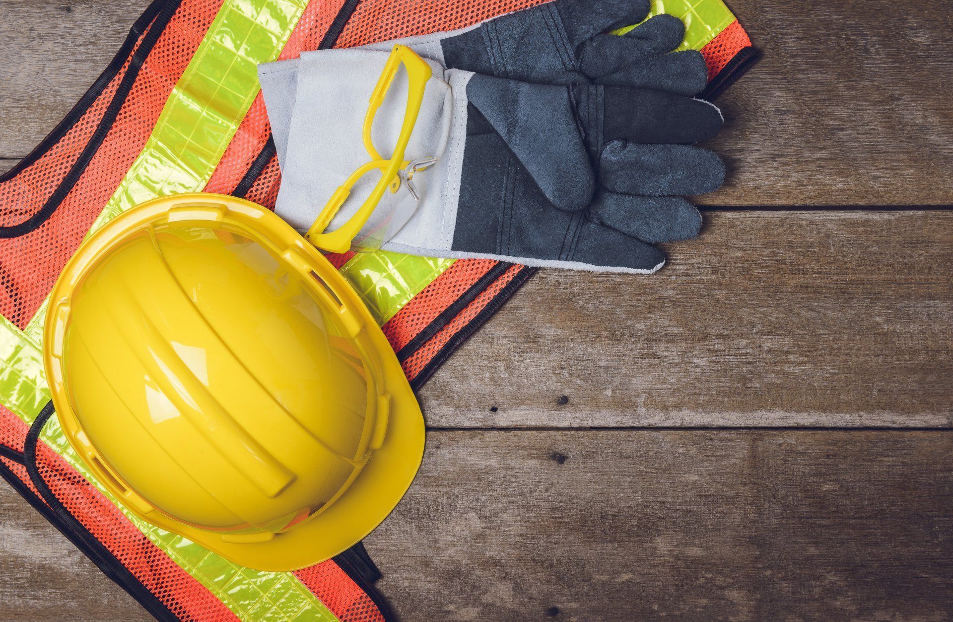Yellow Hard Hat, Safety Vest, Gloves, And Glasses On A Wooden Surface — Wendy's Safety Services in Moulden, NT