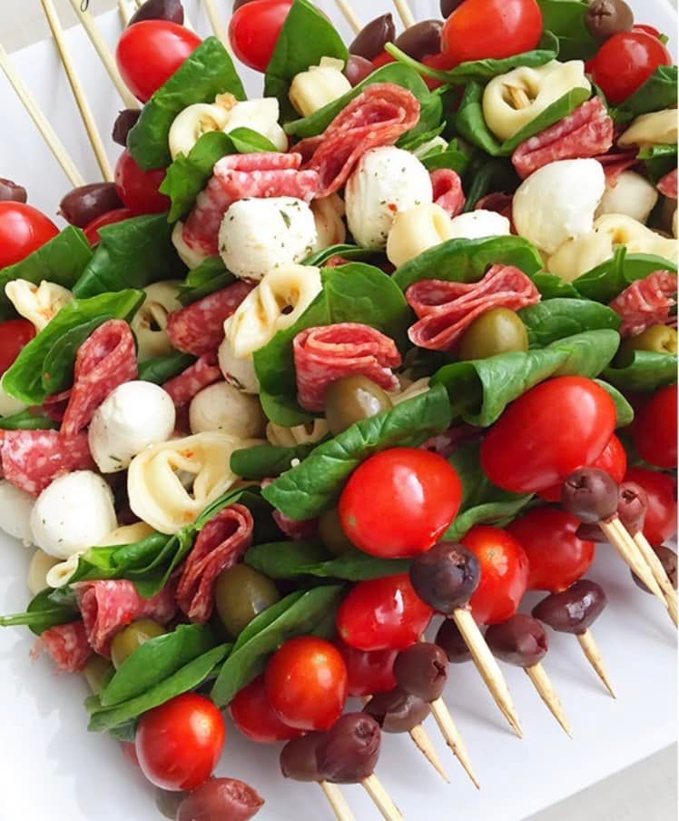 A salad with tomatoes , olives , mozzarella and salami on skewers
