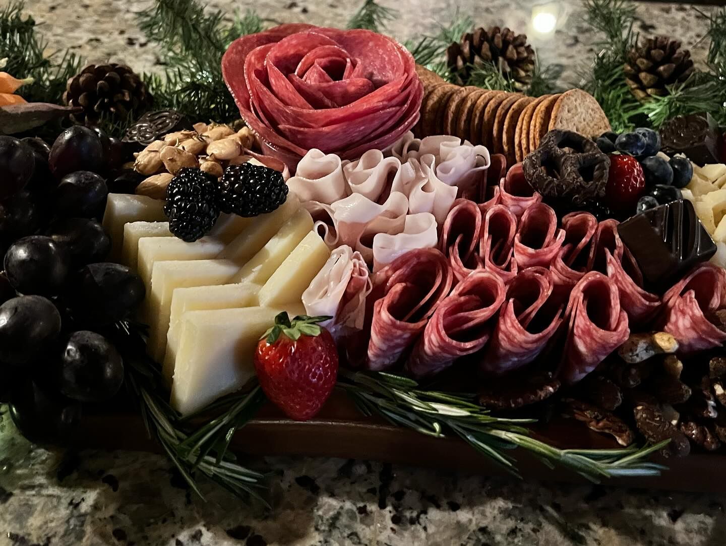 A tray of meats , cheeses , fruits and crackers on a table.