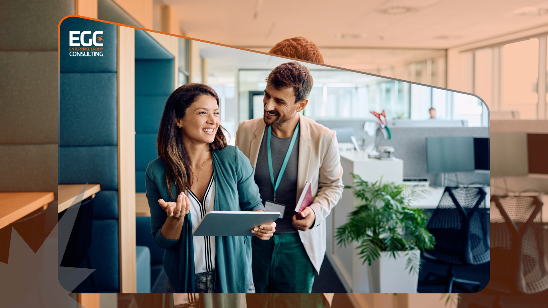 A man and a woman are standing in an office looking at a tablet.
