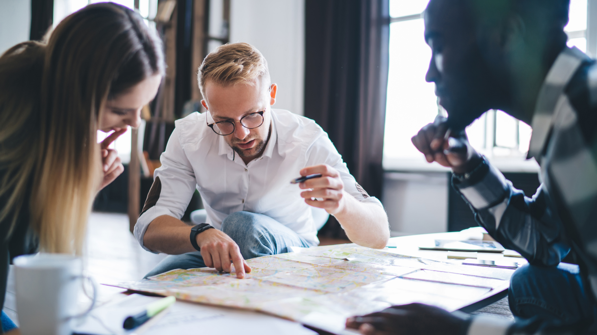 Three coworkers reviewing charts and notes at a table in a bright office
